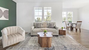 Een woonkamer met een bank, fauteuil, salontafel en een eethoek met stoelen en een tafel.