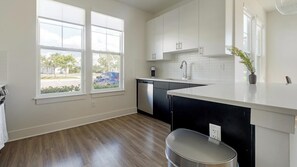 A modern kitchen with white cabinetry, a black countertop, and a view of the street through large windows. - Landing | Modern 2BD, Game Room, Gym (Cape Coral)