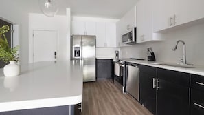 A modern kitchen with white cabinets, stainless steel appliances, and a wooden floor. - Landing | Incredible 1BD, Gym, Game Room (Cape Coral)