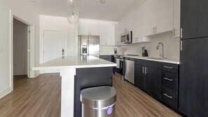Een moderne keuken met een centraal eiland, roestvrijstalen apparatuur en een combinatie van witte en donkere kastjes.