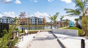 A waterfront patio with a view of a lake, a pool, and residential buildings in the background. - Landing | Beautiful 1BD, Gym, Game Room (Cape Coral)
