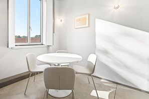 A conference room with a round table and four chairs, a large window with a view of buildings, and a framed map on the wall. - GuestReady-Rou27-G (Porto)