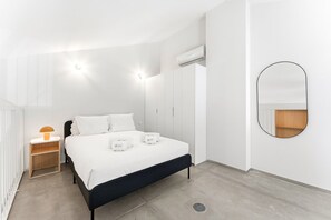 A modern bedroom with a bed, bedside tables, a wardrobe, an air conditioning unit, and a mirror. - GuestReady-Rou27-G (Porto)