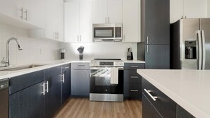 A modern kitchen with stainless steel appliances, white cabinetry, and a wooden floor. - Landing | Chic 1BD, Gym, Game Room (Cape Coral)