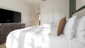 Quarto de hotel com uma cama grande, uma televisão sobre um armário de madeira e uma porta branca ao fundo.