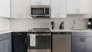 A modern kitchen with stainless steel appliances, white cabinetry, and a tiled backsplash. - Landing | Incredible 1BD, Game Room, Gym (Cape Coral)