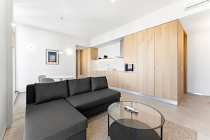 Ein modernes Wohnzimmer mit einer Eckcouch, einem Glastisch und einer Küchenzeile mit Holzschränken.