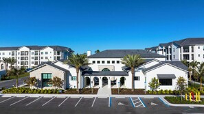 A modern multi-story residential building with a central entrance, parking lot, and surrounding greenery. - Landing | Modern 1BD in East Naples (Naples)