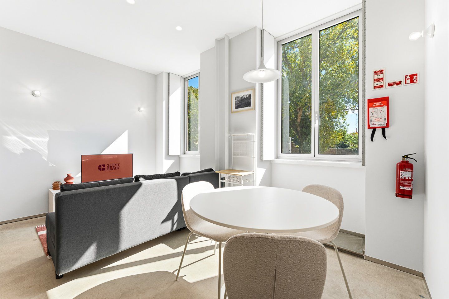 Una habitación moderna con sofá, una mesa redonda y ventana con vista a árboles.