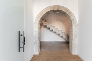 A hallway with a concrete archway leading to a staircase with wooden railings. - GuestReady- Rou27- D (Porto)