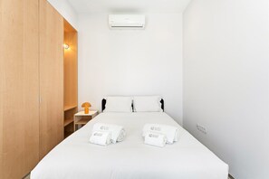 A hotel room with a bed, two pillows, a nightstand with a lamp, a wooden wardrobe, and an air conditioning unit. - GuestReady- Rou27- D (Porto)