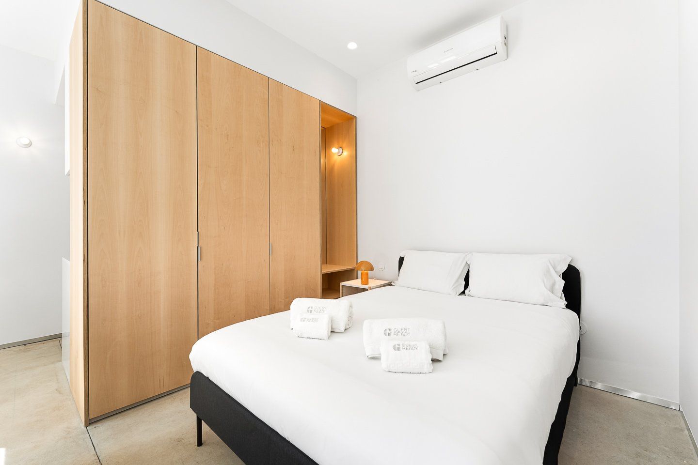 Una habitación de hotel moderna con cama, armario, mesita de noche y aire acondicionado.