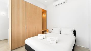 Una habitación de hotel moderna con cama, armario, mesita de noche y aire acondicionado.