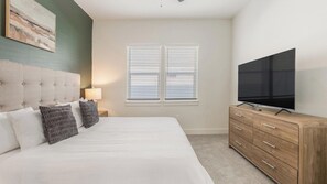A bedroom with a large bed, a television on a wooden dresser, and a window with blinds. - Landing | Stylish 2BD, Gym (Palmetto)