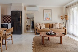 A modern living room with a sofa, coffee table, and dining area. - Salted Sun with pool, spa & fire pit (Manyana)