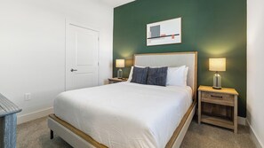 A hotel room with a bed, two bedside tables, a nightstand, a door, and a wall-mounted picture. - Landing | Beautiful 2BD, Gym (Palmetto)