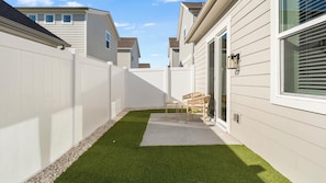 Ein wohnlicher Garten mit Rasenteppich, einer Terrassenfläche und einem weißen Zaun.