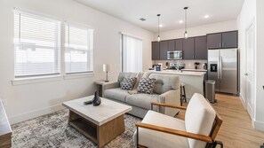 Ein modernes Wohnzimmer mit Sofa, Couchtisch und Essbereich, im Hintergrund eine Küche.