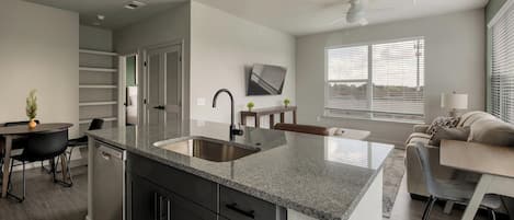 A modern kitchen with a double sink, dark cabinetry, and a dining area with a table and chairs.