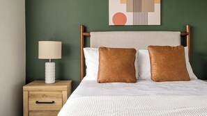 A neatly made bed with two pillows, a bedside lamp, and a wooden nightstand with a drawer. - Landing | Stylish 2BD, Gym, Pool (Mission Bend)