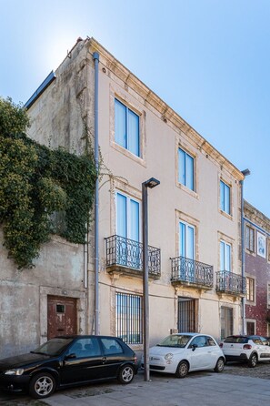 A multi-story building with a balcony on the second floor, a street lamp, and parked cars. - GuestReady- Rou2-E (Porto)