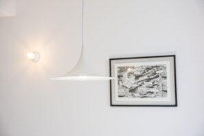 Abstract kunstwerk in een lijst op een witte muur, met een hanglamp.