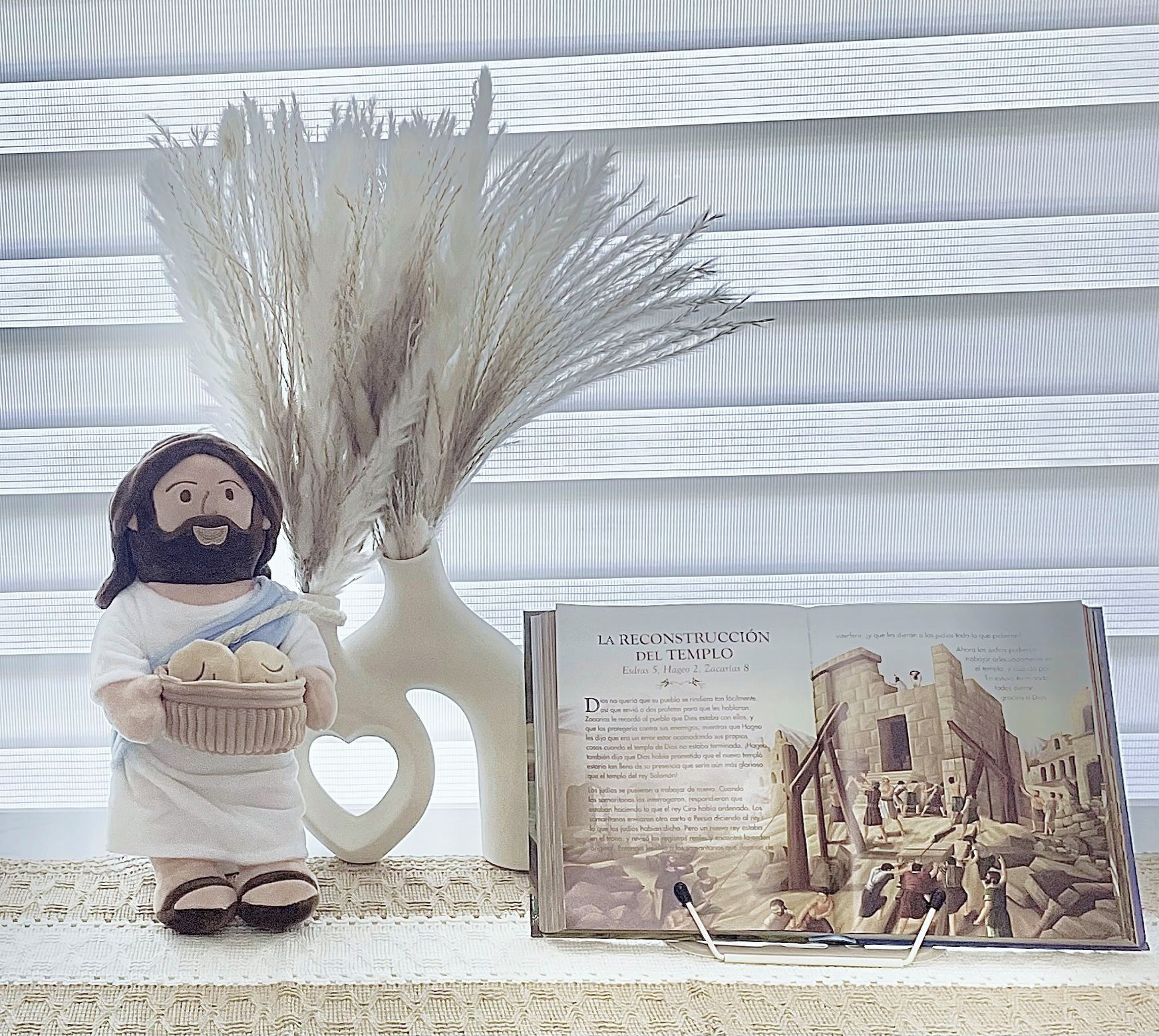 Een decoratief figuurtje met een mand, een witte vaas met gedroogde planten, en een boek getiteld 'LA RECONSTRUCCION DEL TEMPLE' met een afbeelding van tempelruïnes.