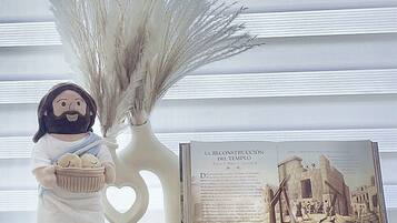 Een decoratief figuurtje met een mand, een witte vaas met gedroogde planten, en een boek getiteld 'LA RECONSTRUCCION DEL TEMPLE' met een afbeelding van tempelruïnes.