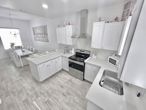 Een moderne keuken met witte kasten, een centraal eiland, roestvrijstalen apparatuur en een zithoek met een bank en tafel.
