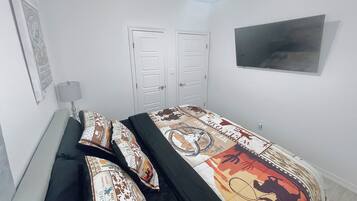 Een slaapkamer met een bed, twee deuren, een lamp en een televisie.