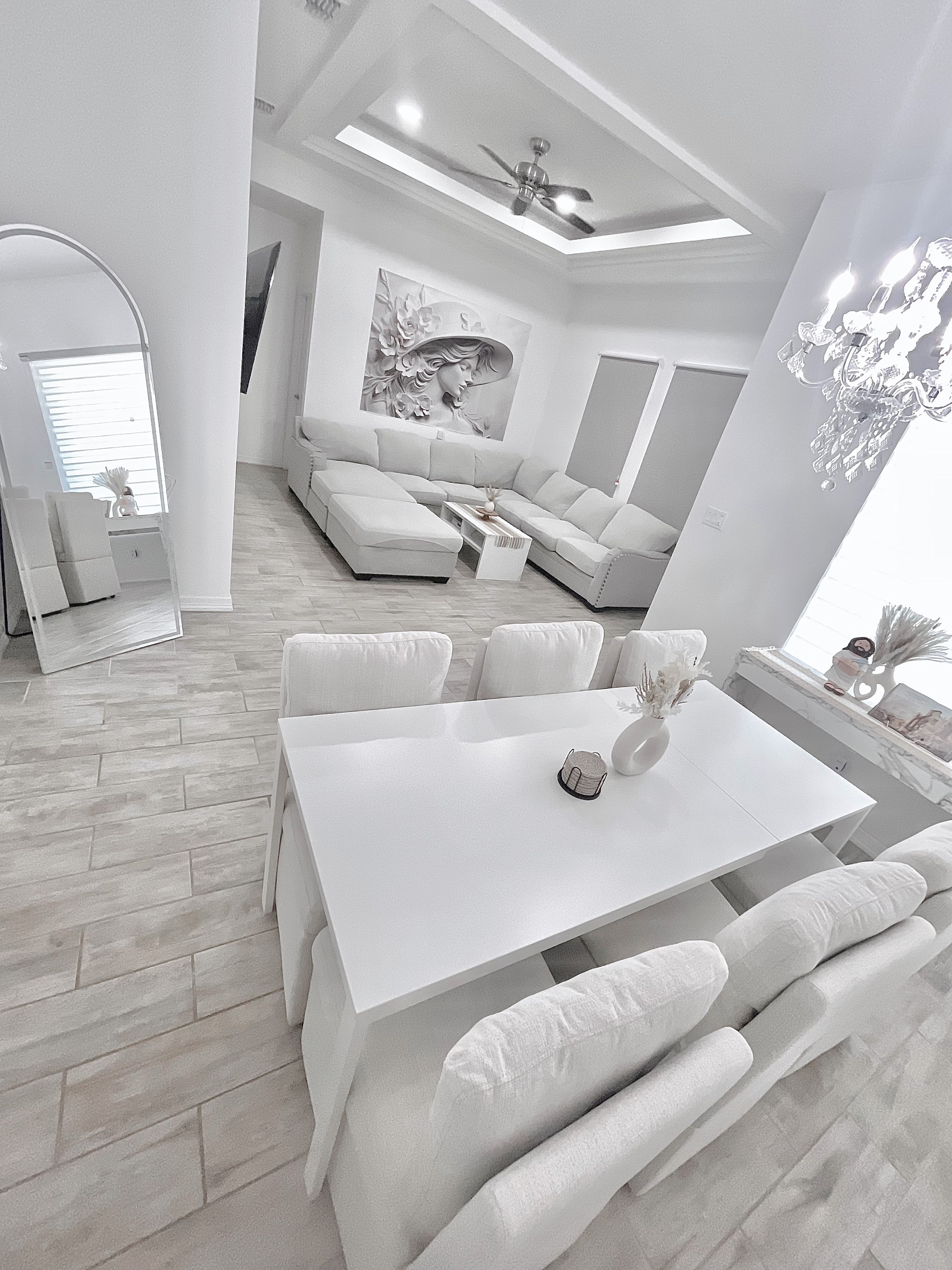 Een moderne woonkamer met een witte bank, een eettafel met stoelen en een plafondventilator.