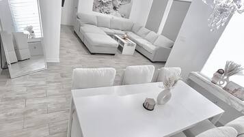 Een moderne woonkamer met een witte bank, een eettafel met stoelen en een plafondventilator.