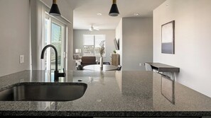 A modern kitchen with a granite countertop, a black faucet, and a dining area with a round table and chairs. - Landing | Stylish 2BD, Gym, Pool (Mission Bend)