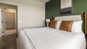 A hotel room with a large bed, a nightstand with a lamp, and a green accent wall. - Landing | Stylish 2BD, Gym, Pool (Mission Bend)