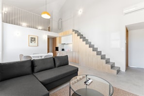 A modern living room with a sofa, a glass coffee table, and a staircase leading to an upper level. - GuestReady- Rou 27-F (Porto)