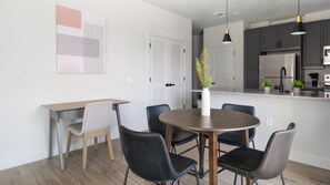 A modern kitchen with dark cabinets, a stainless steel refrigerator, and a black pendant light. - Landing | Modern 2BD, Pool, Gym (Mission Bend)