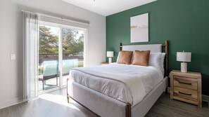 A bedroom with a bed, two bedside tables, a sliding glass door, and a green accent wall. - Landing | Chic 2BD, Gym, Pool (Mission Bend)