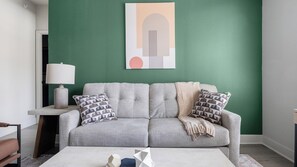 A living room with a grey sofa, patterned cushions, a white coffee table, and a lamp on a side table. - Landing | Chic 2BD, Gym, Pool (Mission Bend)