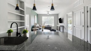 A modern kitchen with granite countertops, a built-in sink, pendant lighting, and a dining area with a round table. - Landing | Chic 2BD, Gym, Pool (Mission Bend)