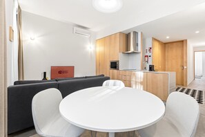 Ein modernes Hotelzimmer mit einer Couch, einem runden Esstisch, einer Küchenzeile und einem Schild mit der Aufschrift 'GUEST READY'.