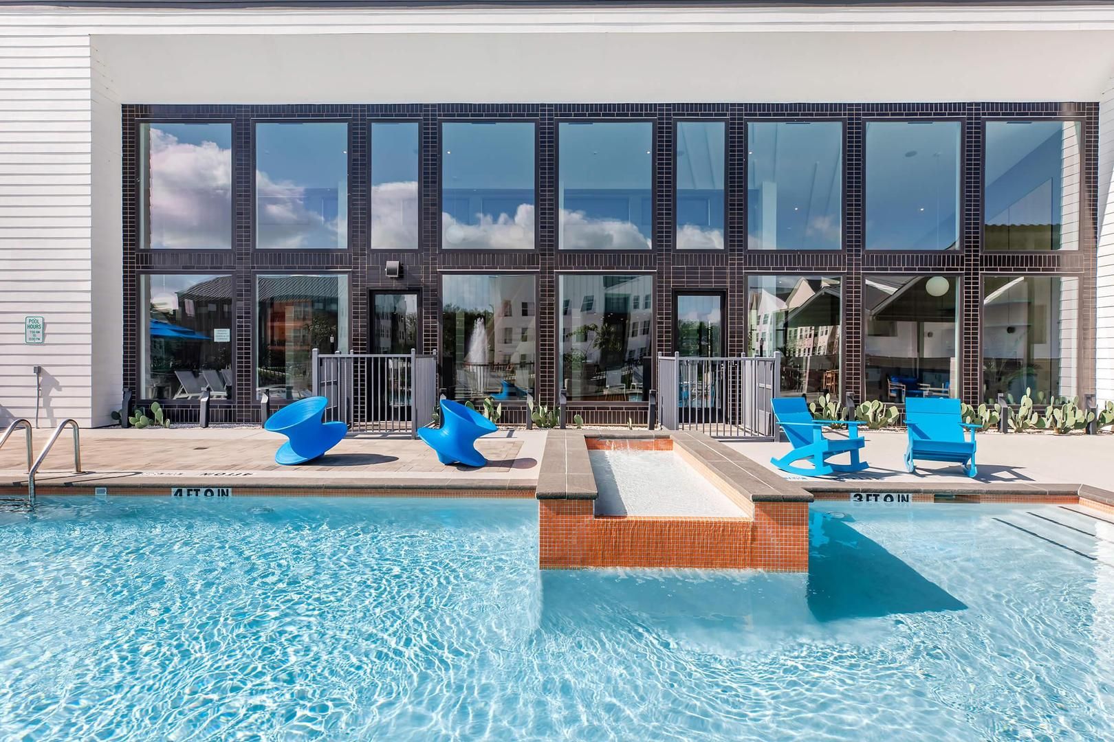 A modern building with a pool area featuring blue chairs and a clear view of the sky.