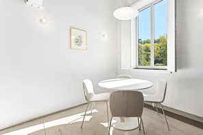 Ein moderner Konferenzraum mit rundem Tisch und vier Stühlen, einem großen Fenster mit Blick auf Grünflächen und einem gerahmten abstrakten Kunstwerk an der Wand.