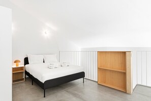 Ein modernes Schlafzimmer mit einem schwarzen Bett, weißer Bettwäsche, einem Nachttisch aus Holz mit einer Lampe und einer eingebauten Holzregaleinheit.