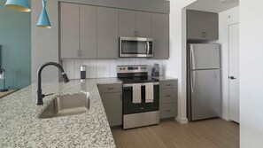 A modern kitchen with stainless steel appliances, a granite countertop, and grey cabinetry. - Landing | Spectacular 1BD in Sunnyside (Houston)