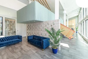 A spacious lobby with two blue sofas, a potted plant, and a modern staircase. - Landing | Spectacular 1BD in Sunnyside (Houston)