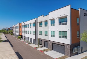 A modern multi-story residential building with a row of garages and a parking area. - Landing | Spectacular 2BD, Gym (Phoenix)