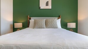A bed with white bedding, two patterned pillows, and two bedside lamps against a green wall. - Landing | Incredible 1BD in Loughman (Davenport)