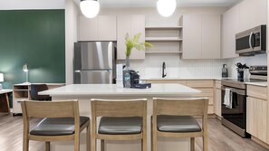 A modern kitchen with a central island, stainless steel appliances, and wooden chairs. - Landing | Incredible 1BD in Loughman (Davenport)