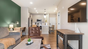 A modern living room with a sofa, coffee table, and a dining area with a table and chairs. - Landing | Incredible 1BD in Loughman (Davenport)