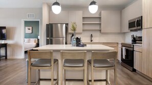 A modern kitchen with a central island, stainless steel appliances, wooden chairs, and pendant lighting. - Landing | Stylish 2BD in Loughman (Davenport)